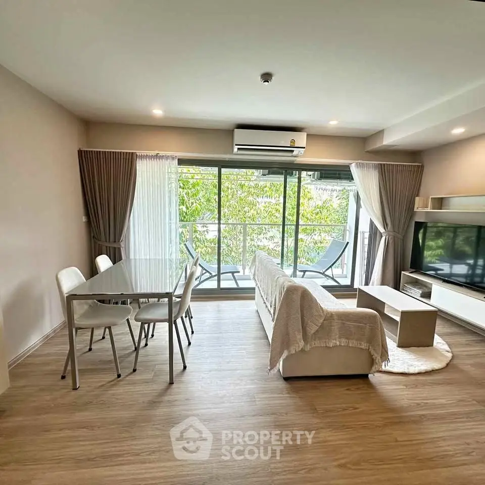 Modern living room with large windows and balcony view, featuring stylish furniture and open layout.