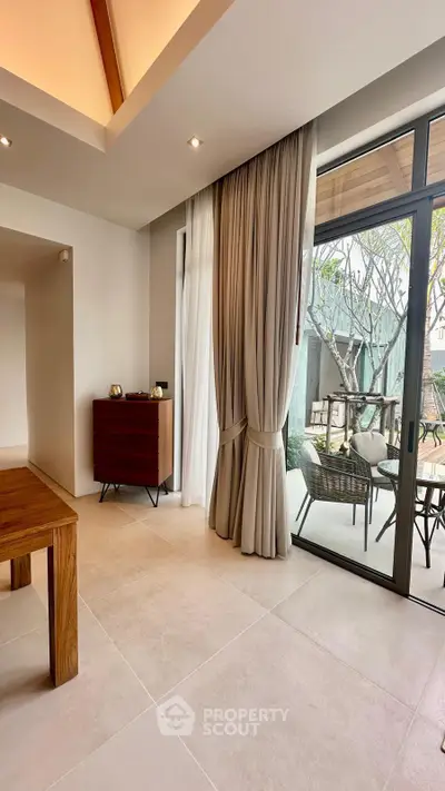 Spacious modern living area with large windows and elegant curtains opening to a stylish outdoor patio.