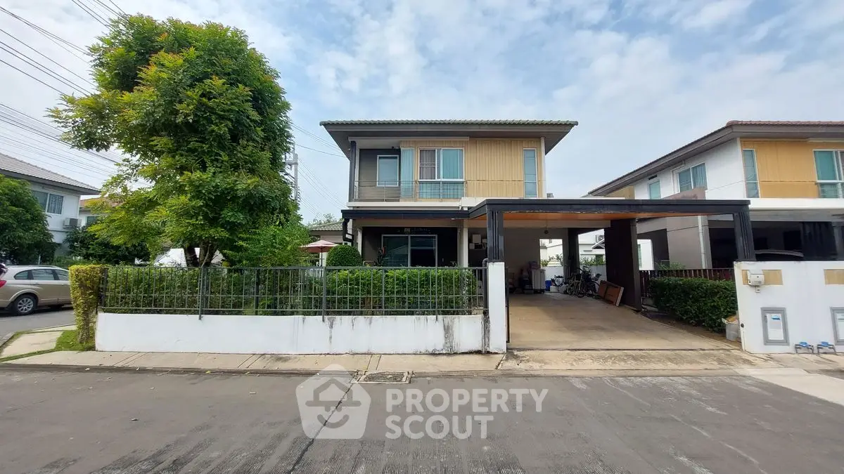 Modern two-story house with carport and lush greenery in suburban neighborhood.