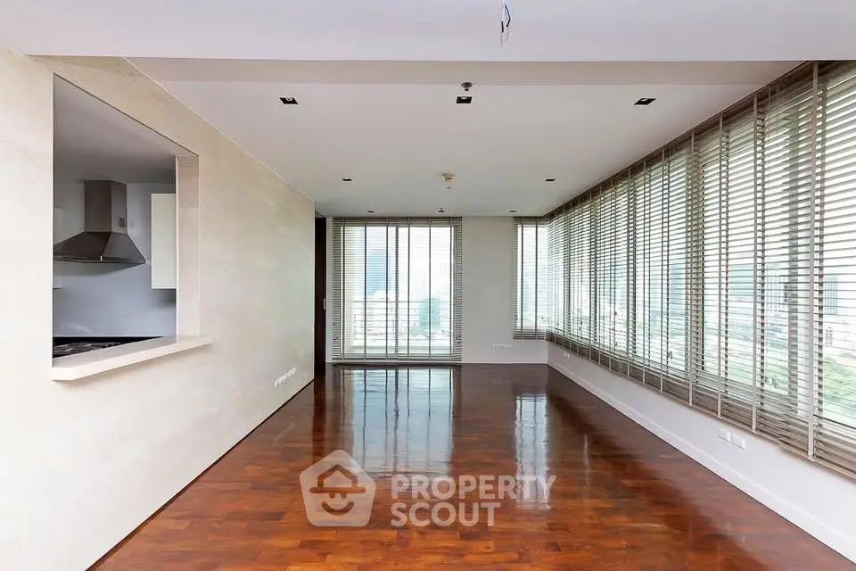 Spacious modern living room with large windows and wooden flooring, offering abundant natural light and city views.
