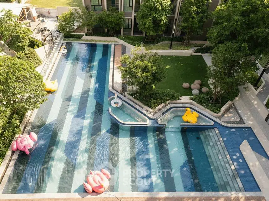 Luxurious outdoor pool area with lush greenery and playful floaties in a modern residential complex.