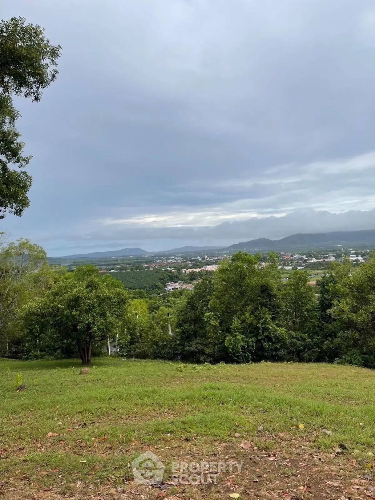 Scenic view of lush green landscape with distant town and mountains under cloudy sky