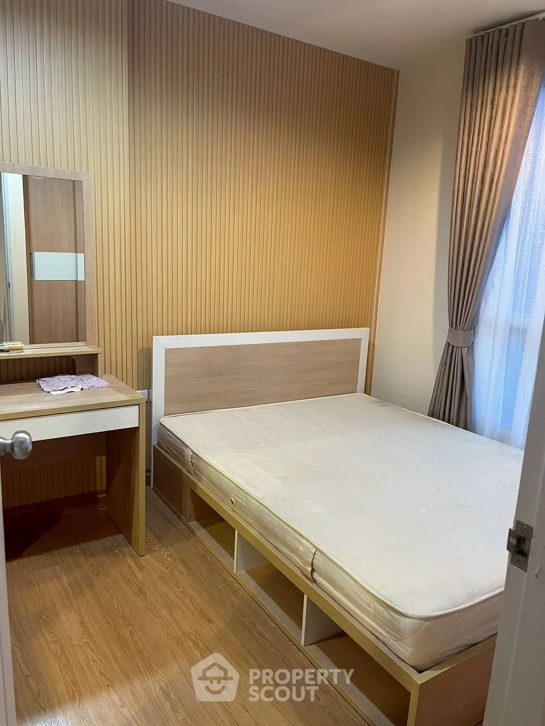 Cozy bedroom with wooden accents and natural light, featuring a bed and vanity desk.