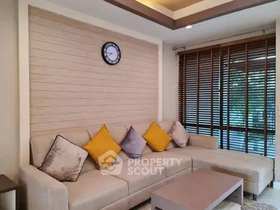 Stylish living room with modern beige sofa and vibrant cushions, featuring elegant wooden blinds and wall clock.