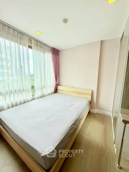 Bright and airy bedroom with large window and modern furnishings in a high-rise apartment.