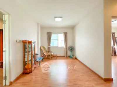 Spacious living area with wooden flooring and natural light, featuring a cozy seating corner.