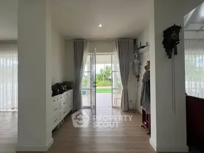Spacious living area with elegant decor and garden view, featuring large windows and wooden flooring.