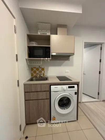 Compact kitchen with washing machine and microwave in modern apartment