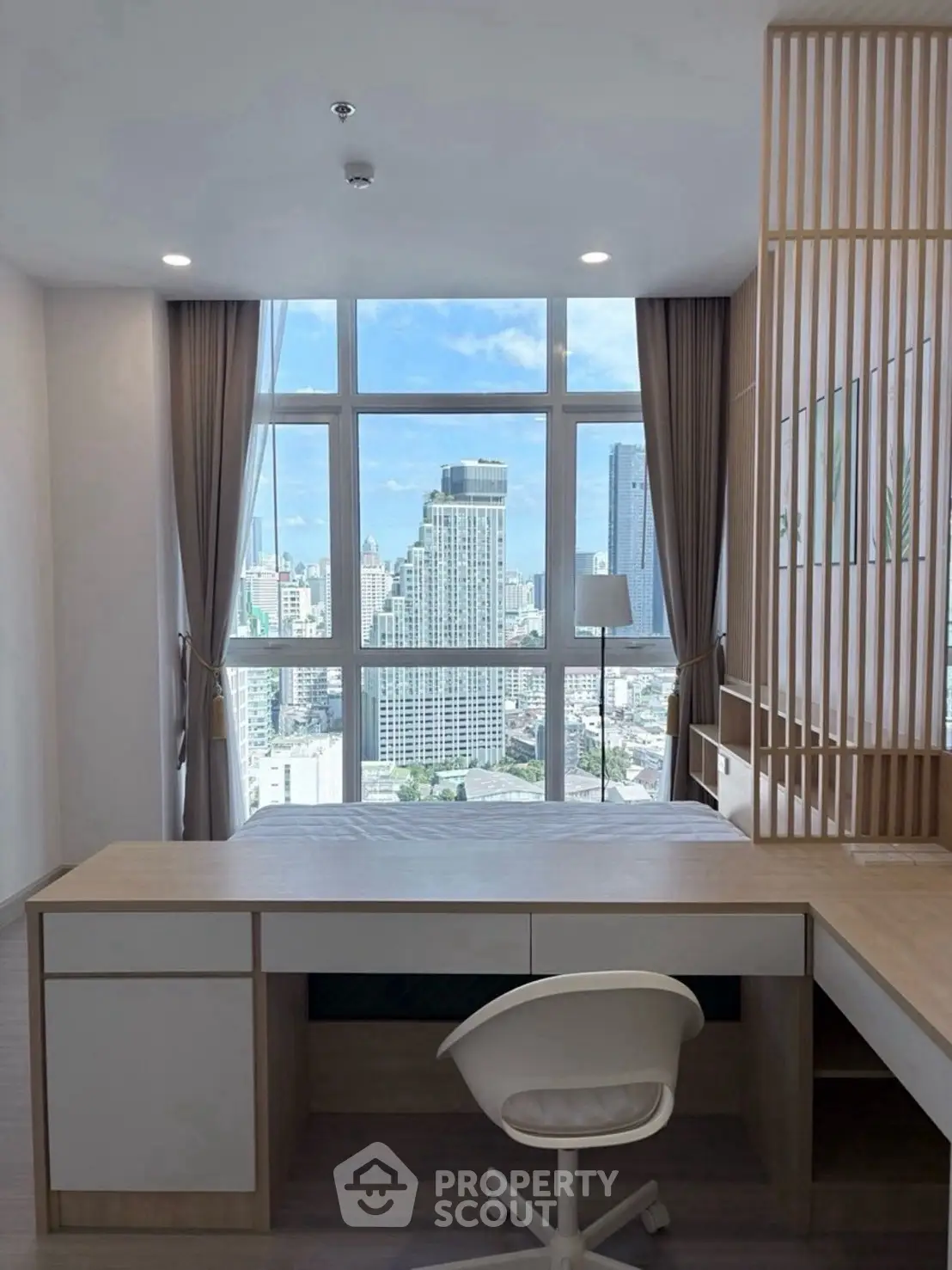 Modern bedroom with city view, featuring sleek desk and chair, large window, and stylish decor.