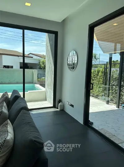 Modern living room with pool view and sleek interior design, featuring large windows and contemporary decor.