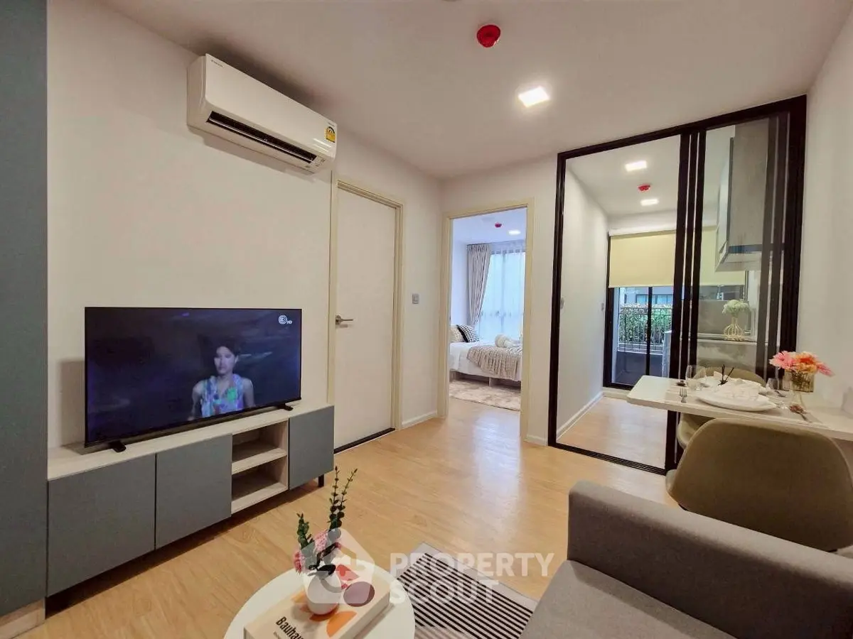 Modern living room with TV, air conditioning, and view into bedroom, featuring stylish decor and open layout.