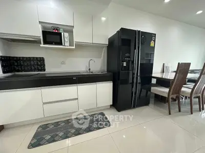 Modern kitchen with sleek black fridge and dining area in open layout apartment.