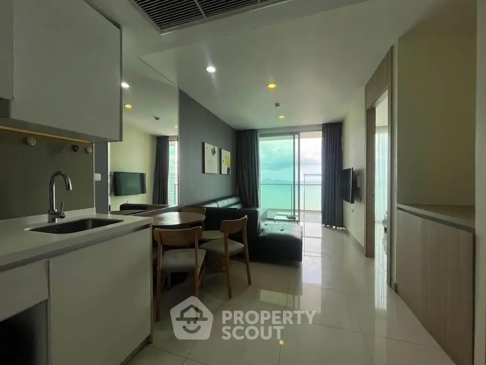 Modern living room with ocean view, sleek furniture, and open kitchen layout.