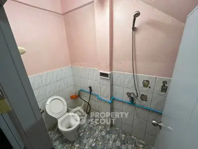 Compact bathroom with pink walls and tiled flooring, featuring a toilet and shower setup.