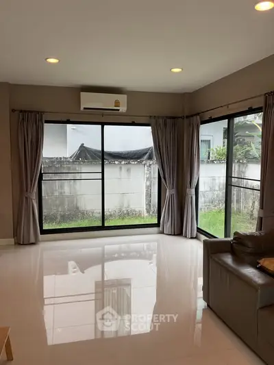 Spacious living room with large windows and garden view, featuring modern air conditioning and elegant curtains.