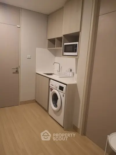 Modern compact kitchen with integrated washing machine and microwave in sleek cabinetry.