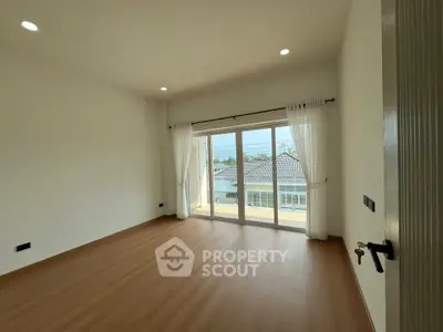 Spacious empty room with large window and wooden flooring, perfect for customization.