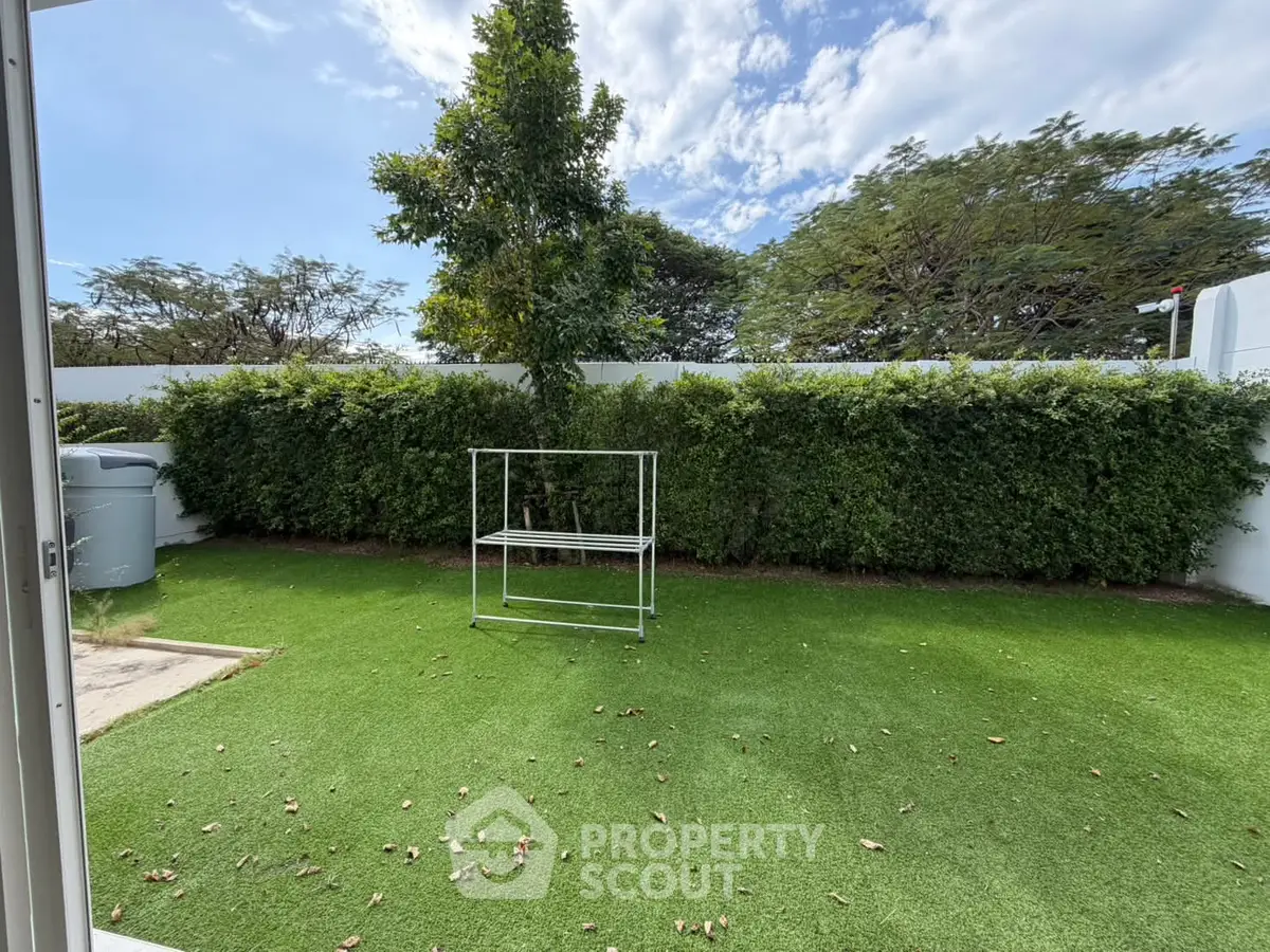 Spacious backyard with lush greenery and artificial grass, perfect for outdoor relaxation.