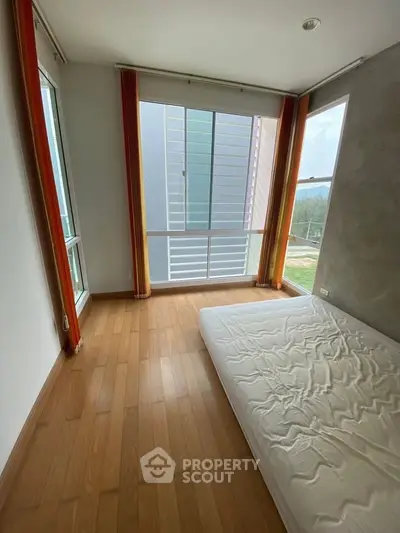 Spacious bedroom with large windows and wooden flooring, offering ample natural light.