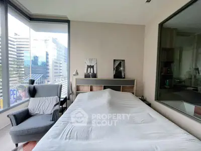 Modern bedroom with large windows offering city views, featuring a cozy armchair and stylish decor.