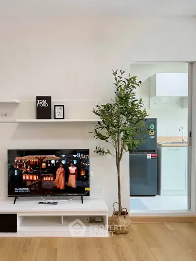 Modern living room with TV and open kitchen layout, featuring sleek design and natural light.