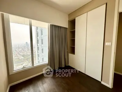 Modern apartment corner with large window and city view, featuring built-in storage and elegant curtains.