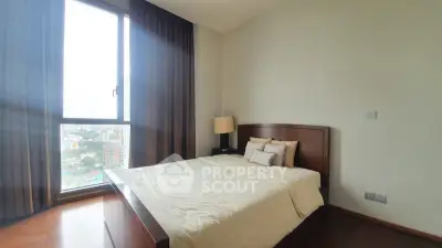 Spacious bedroom with large window offering stunning city views, featuring elegant wooden furniture and cozy ambiance.