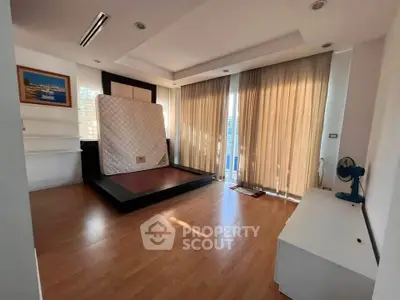 Spacious bedroom with wooden flooring and large windows for natural light.