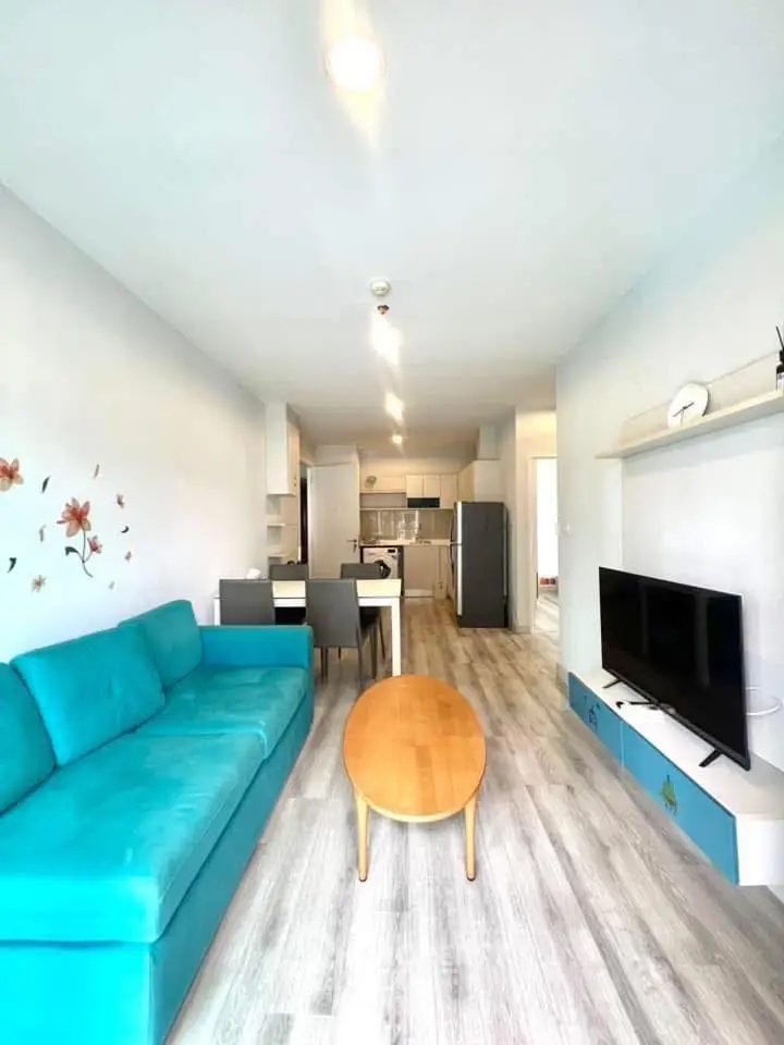 Modern living room with teal sofa, wooden coffee table, and open kitchen layout