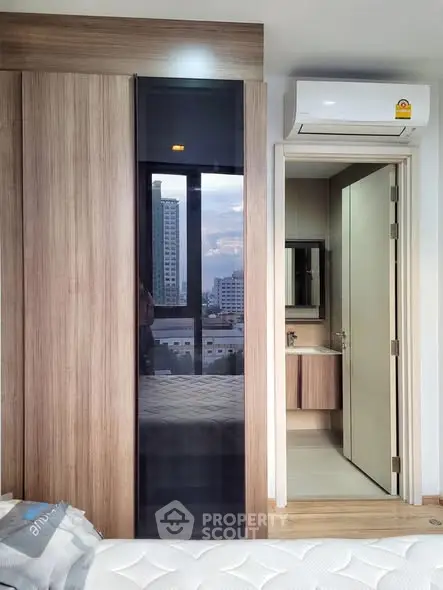 Modern bedroom with sleek wardrobe and ensuite bathroom, featuring city view from window.