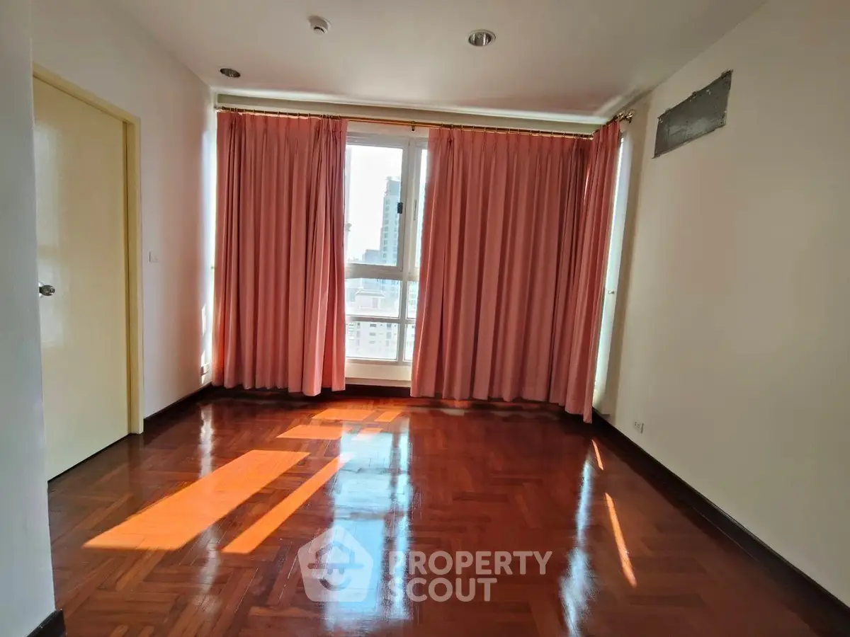 Spacious room with polished wooden floors and large window with pink curtains.