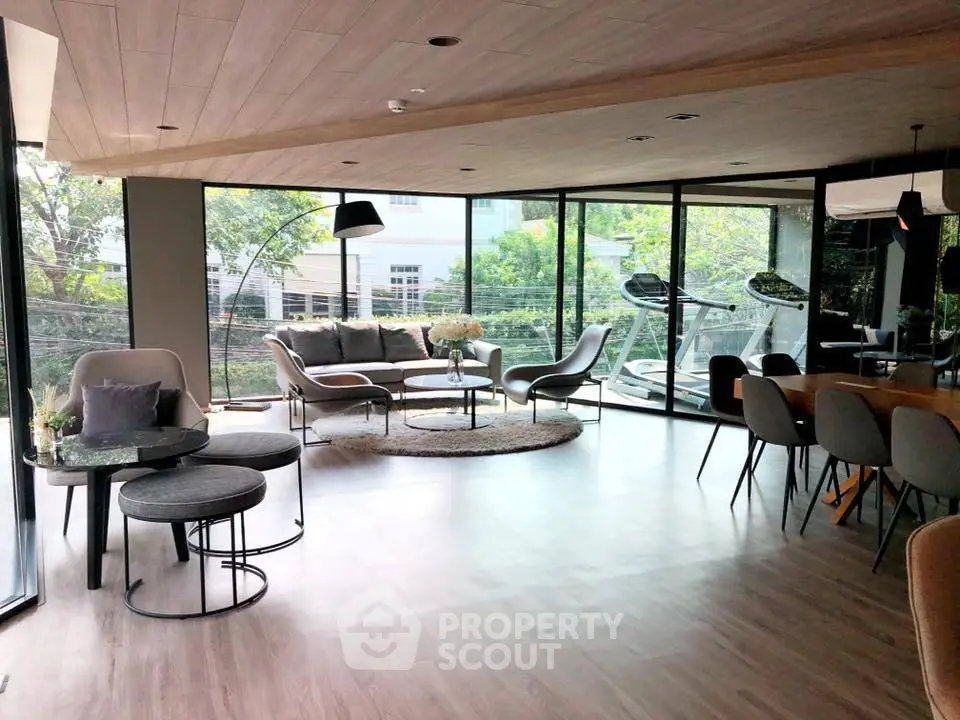 Spacious modern living room with large windows and stylish furniture, offering a serene garden view.