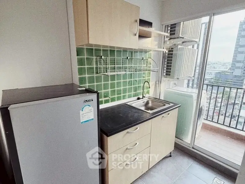 Modern kitchen with green tile backsplash and balcony view in urban apartment.