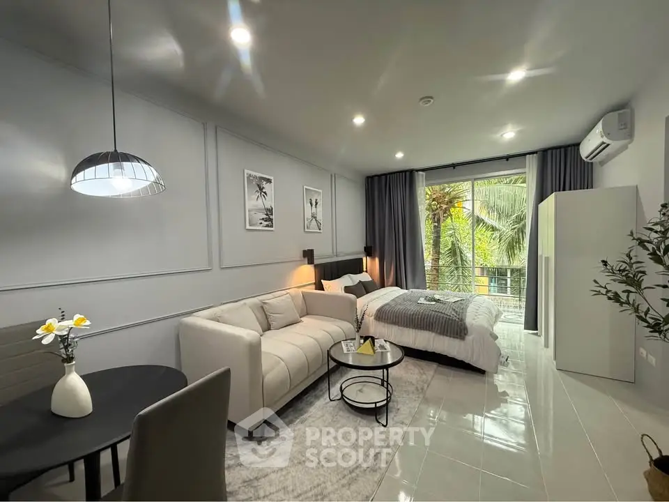 Modern studio apartment with stylish decor and large windows overlooking greenery.
