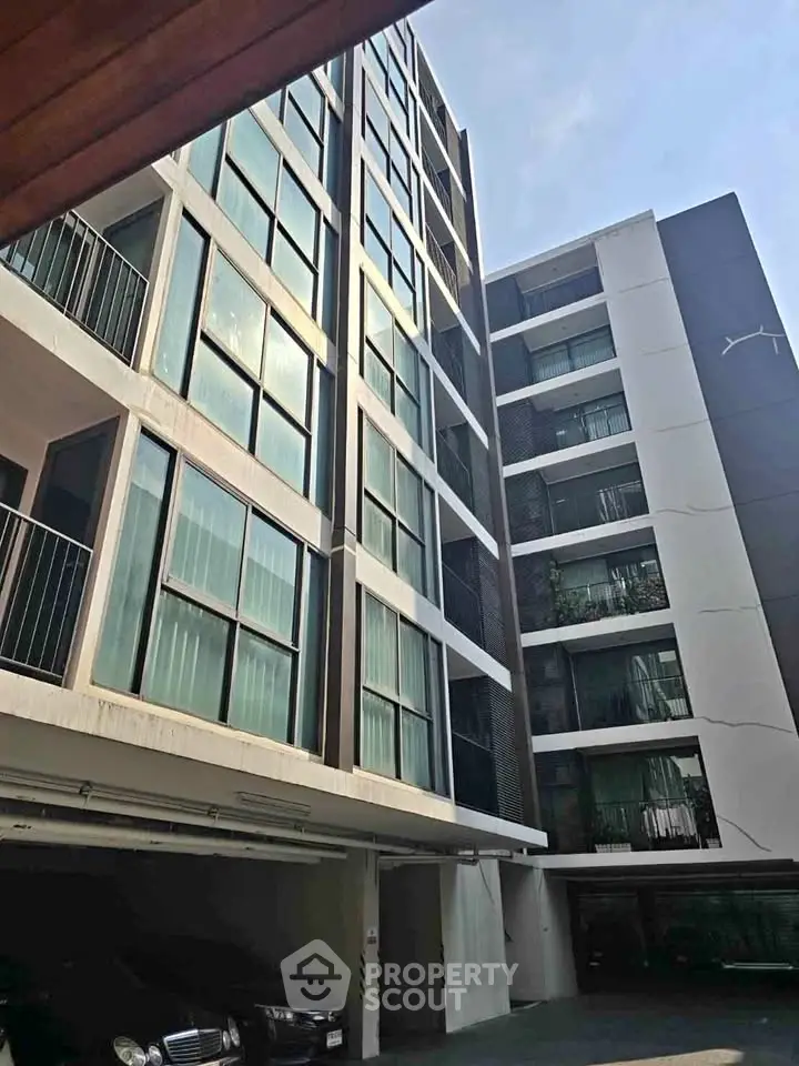 Modern multi-story apartment building with sleek glass facade and parking area.