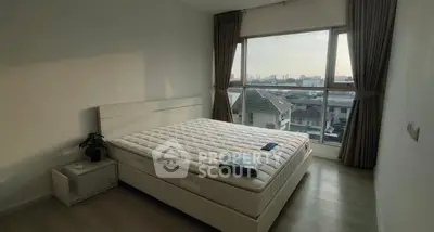 Spacious bedroom with large window offering city view and natural light.