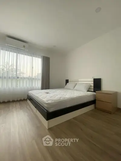 Spacious bedroom with modern design and natural light, featuring a comfortable bed and wooden flooring.