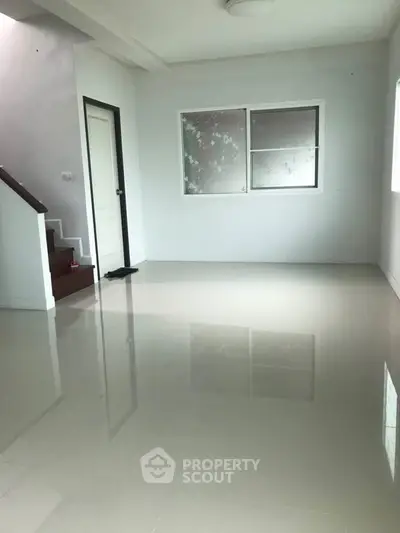 Spacious empty room with glossy tiled floor and staircase, ideal for customization.