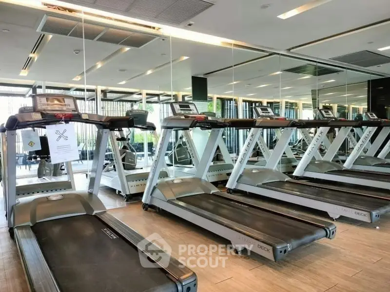 Modern gym with multiple treadmills and mirrored walls in luxury apartment complex.