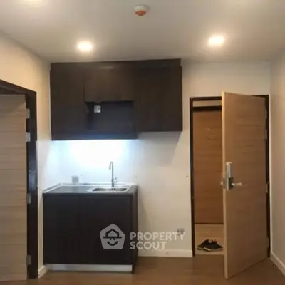 Compact kitchen area with dark cabinets and open door in modern apartment