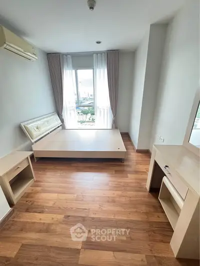 Spacious bedroom with wooden flooring and large window offering city views.