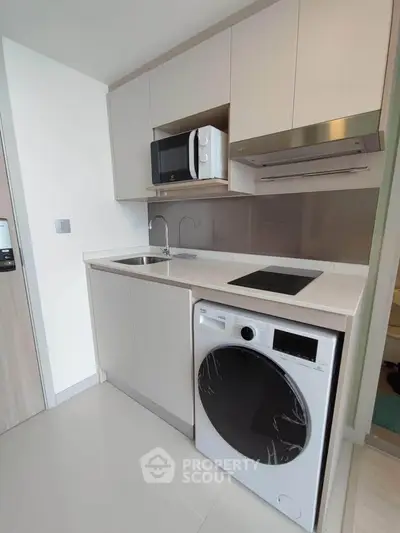 Modern compact kitchen with built-in appliances and washing machine in sleek apartment.
