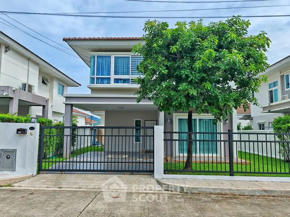 Modern two-story house with lush garden and gated entrance in suburban neighborhood.