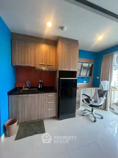 Modern compact kitchen with wooden cabinets and sleek appliances in a bright room with blue accent wall.