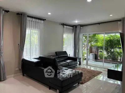 Spacious living room with modern black leather sofas and large windows opening to a lush balcony view.