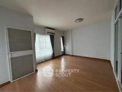 Spacious empty room with wooden flooring and large windows, perfect for customization.