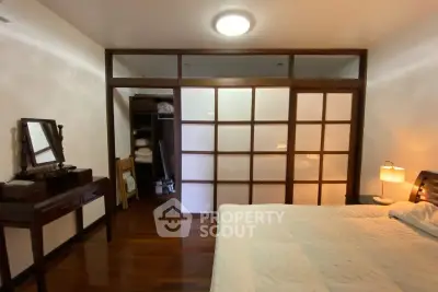 Elegant bedroom with wooden flooring and sliding doors, featuring a cozy bed and stylish furniture.
