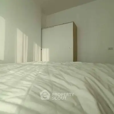 Minimalist bedroom with white bedding and wardrobe, bathed in natural light.