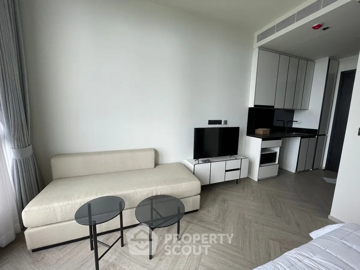 Modern living room with sleek kitchen in open layout, featuring stylish furniture and natural light.