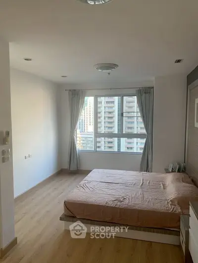 Spacious bedroom with large window offering city view in modern apartment.